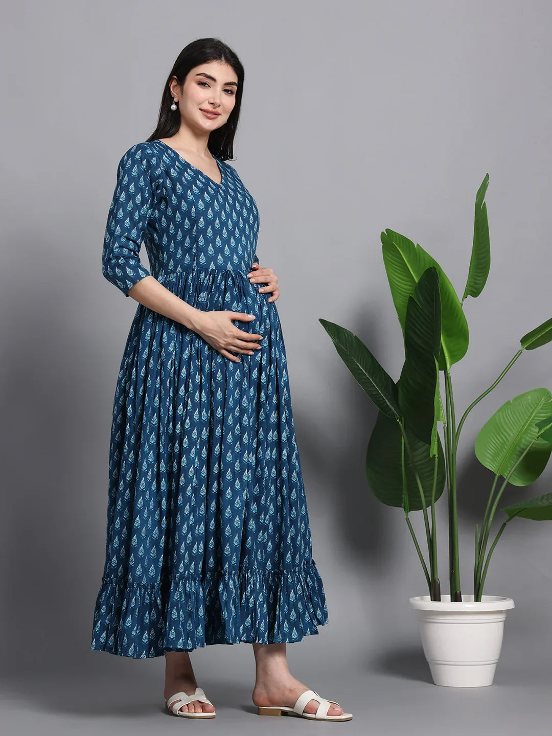 Pregnant woman in blue printed maternity dress with three-quarter sleeves, indoor setting